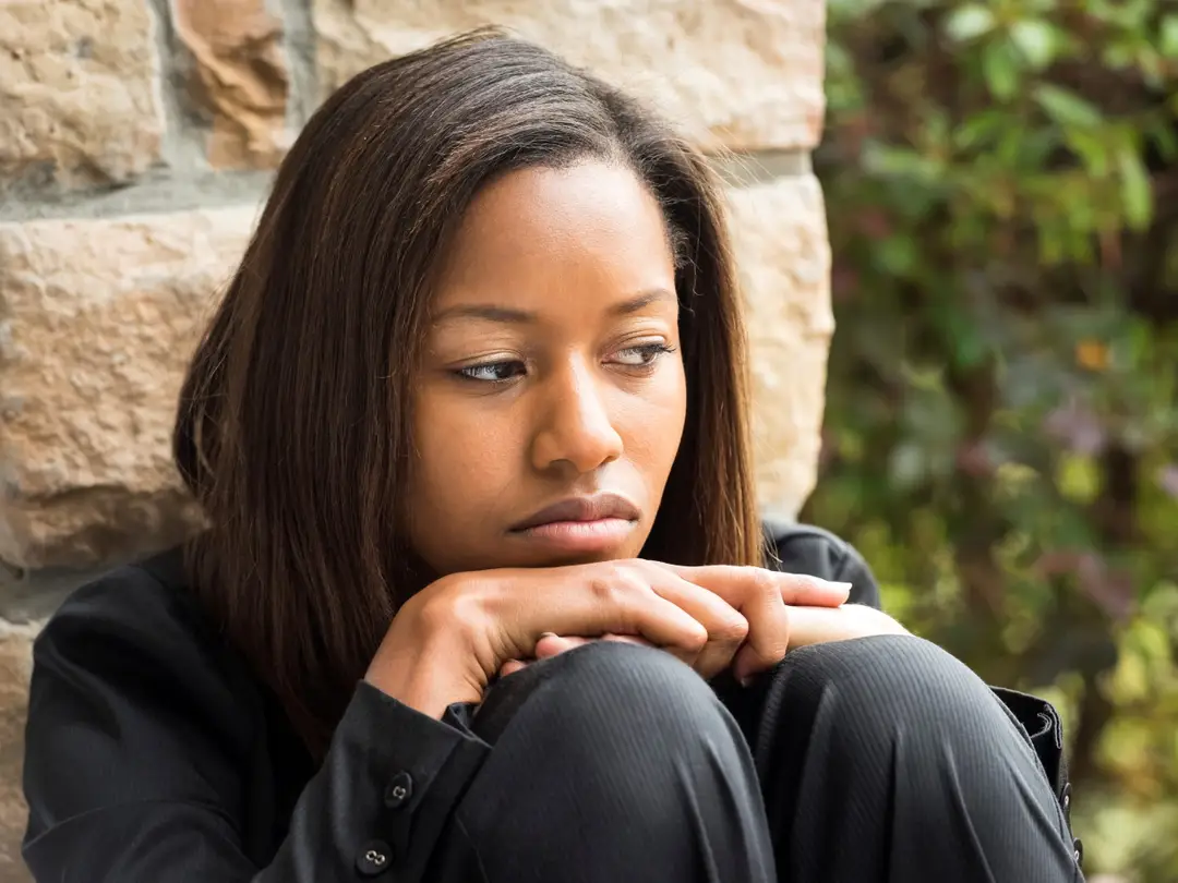 Woman with sad expression sitting with chin resting on knees