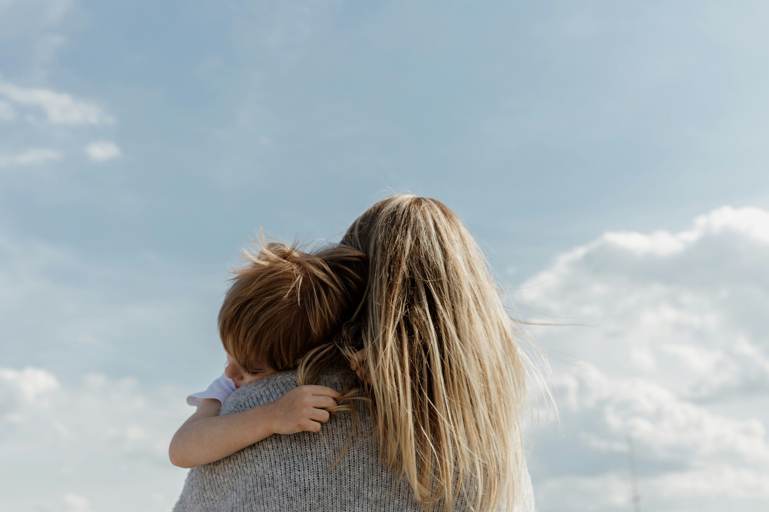 child and family services A woman with long blonde hair holds a child against a blue sky with clouds